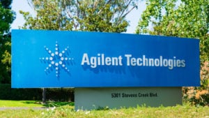 An image of a blue sign on grass in front of trees that has an "Agilent Technologies" logo and the address "5301 Stevens Creek Blvd." on a sunny day.