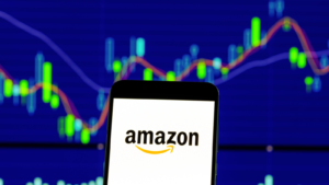 An image on the Amazon logo on a phone, held in front of a stock chart to represent Amazon stock