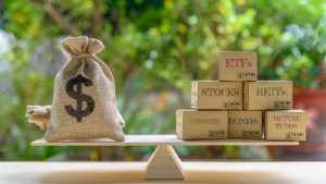 a stock image of a bag of money on a triple beam scale, perfectly balanced with blocks labeled with asset classes such as "REITs" and "ETFs"