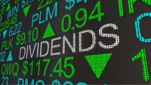 A stock market ticker tape projects the word "DIVIDENDS" in white text. representing dividend stocks to buy