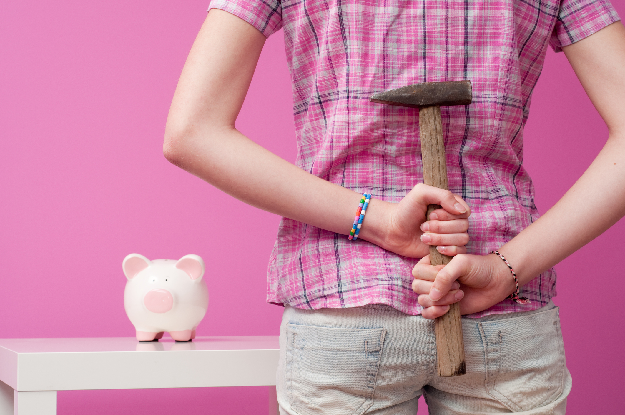 Someone approaching a piggy bank with a hammer behind the back.