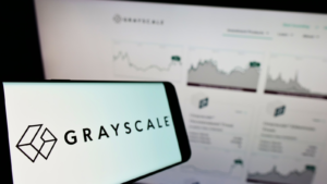 The Grayscale Investments logo is seen on a smartphone in front of a computer screen displaying Grayscale's website.
