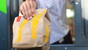 Man holds out a McDonald's bag with the golden arches logo on it at a drive-thru window.