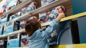 A photograph of a child reaching for a toy truck on a shelf in a store.
