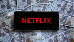 Netflix (NFLX) logo displayed on smartphone on top of pile of money.