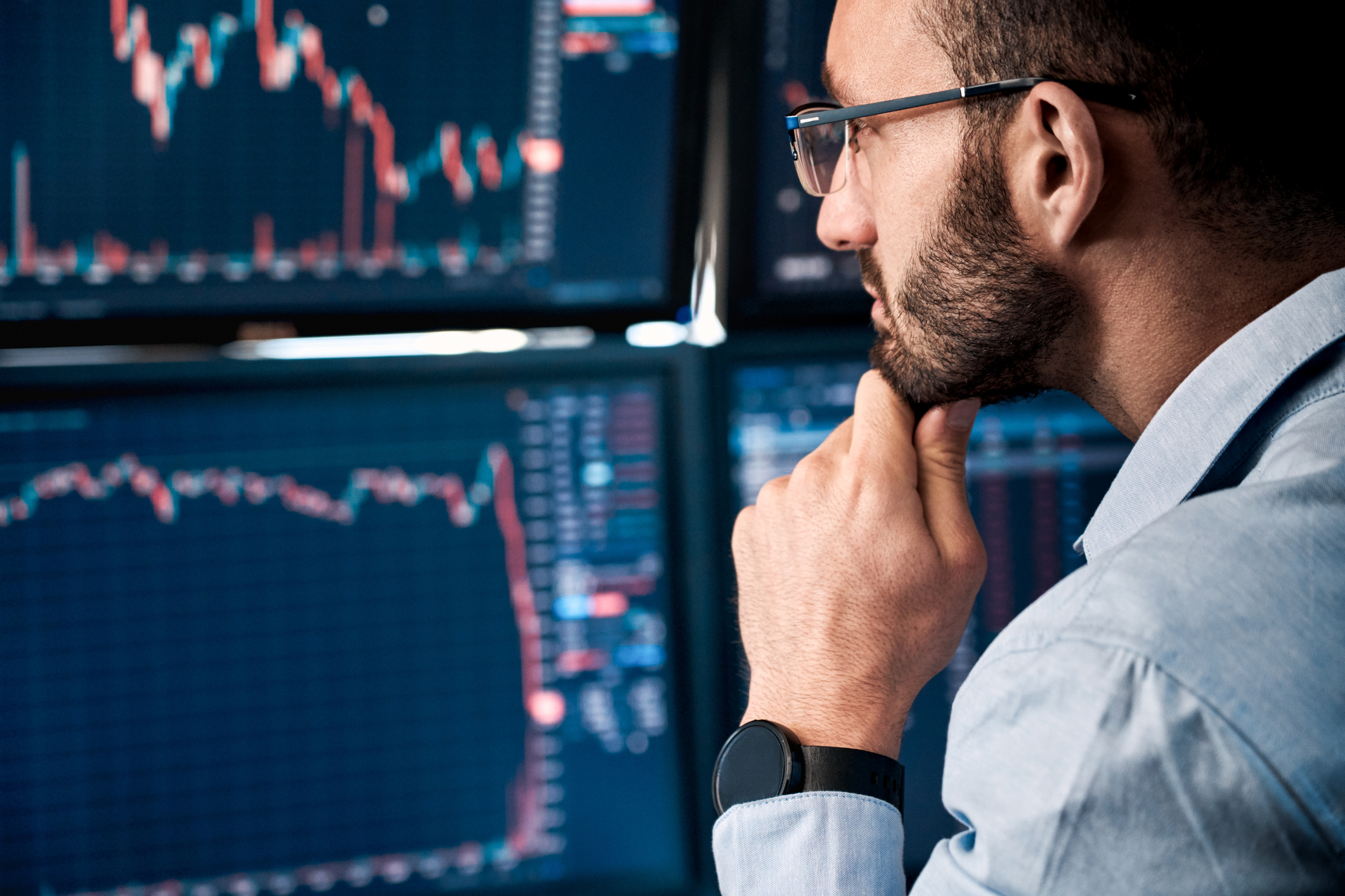 Trader pondering while looking at stock charts on monitors. 