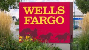 Wells Fargo (WFC) bank sign in yellow and red with wagon logo. The sign is flanked by tall grass