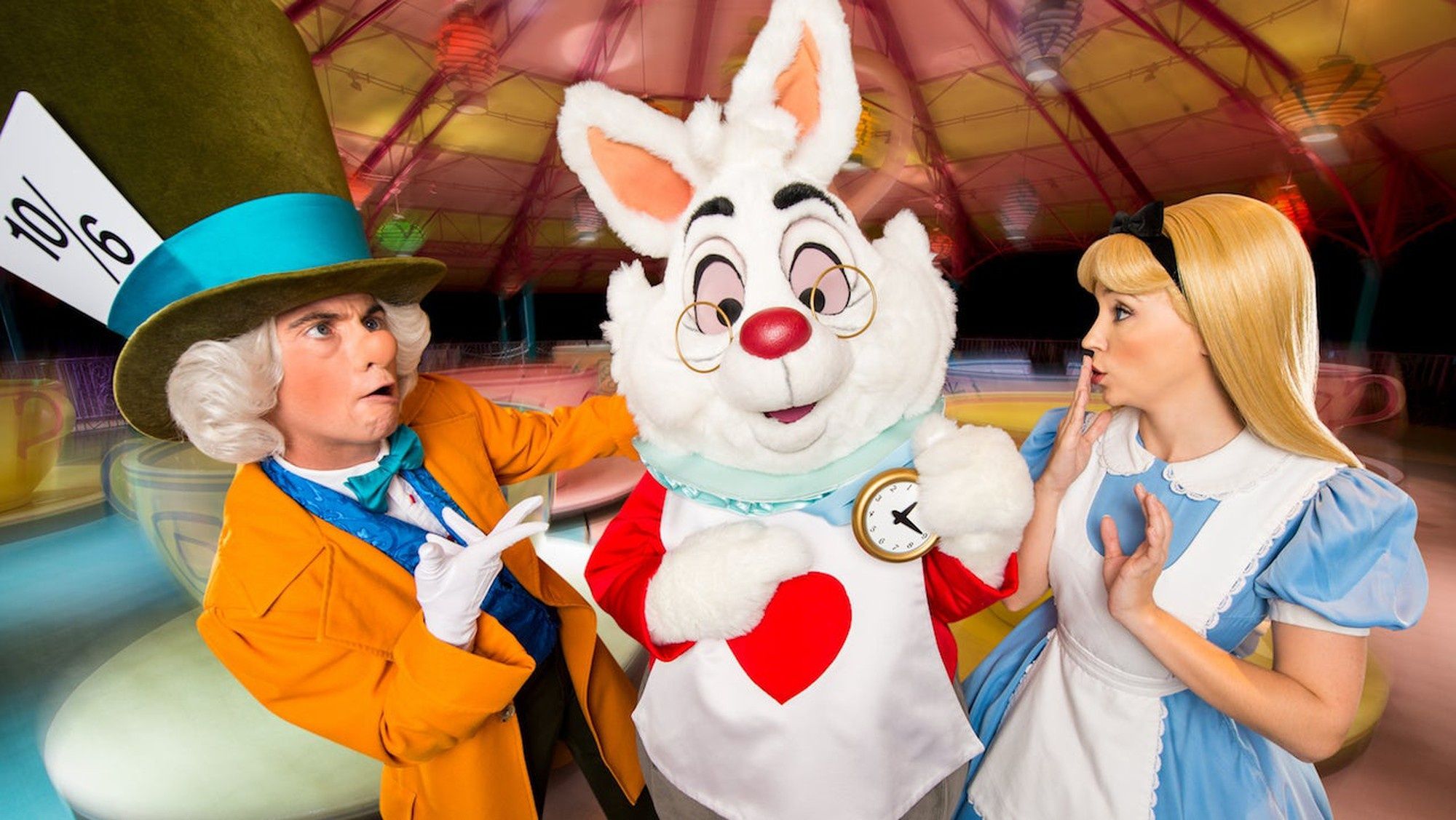 Alice, Rabbit, and Mad Hatter look puzzled in front of their spinning teacup ride at Disney World.