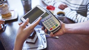 a person holding a smartphone over a check out scanner representing payments stocks to buy