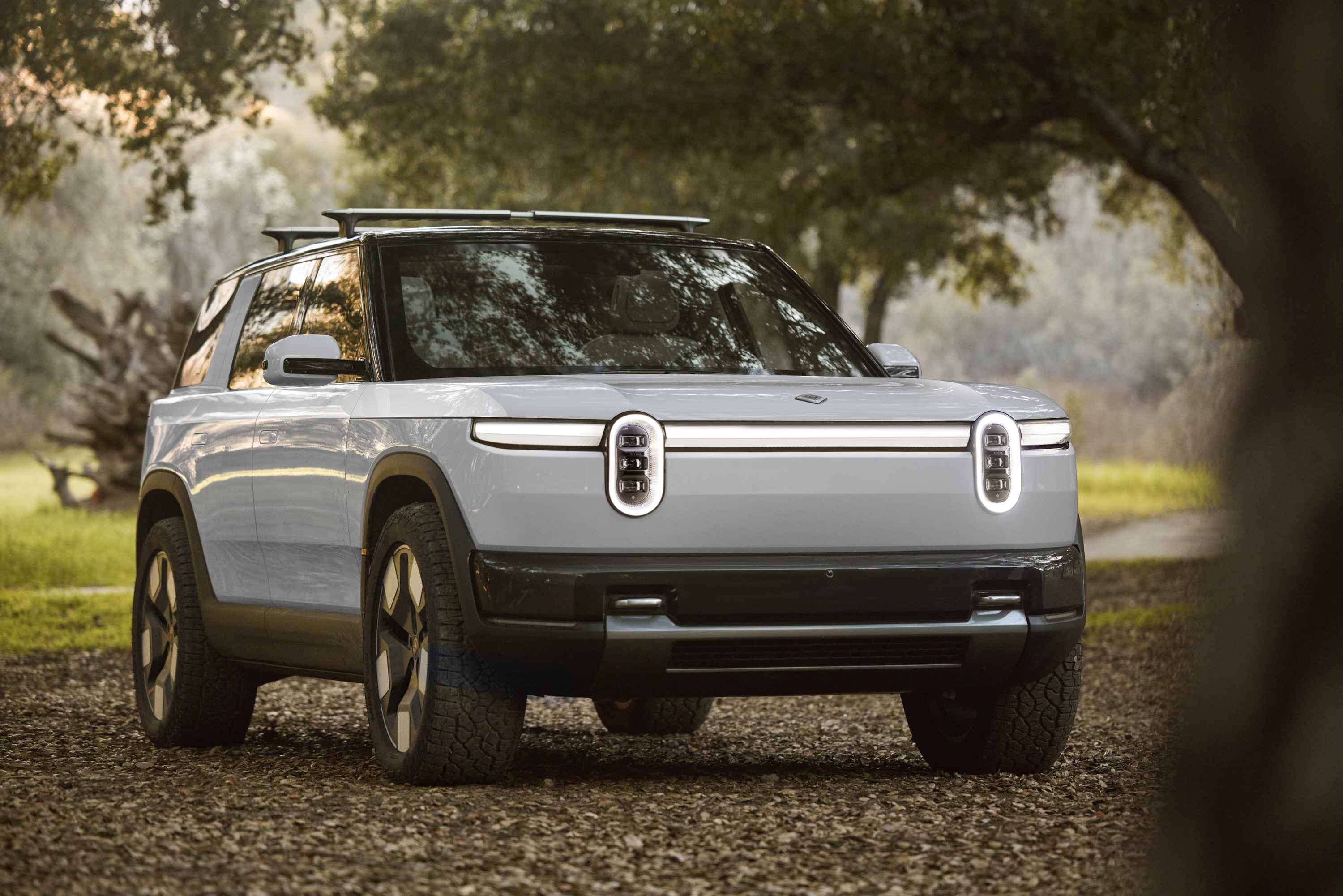 A gray Rivian R2, a rugged midsize electric SUV, in a forest setting. 