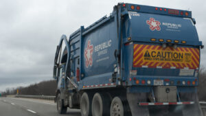 An image of a blue Republic Services trash truck driving on the highway on a cloudy day.