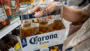 An image of a person holding a Corona Extra bottles six pack in front of a shelf in the beer section.