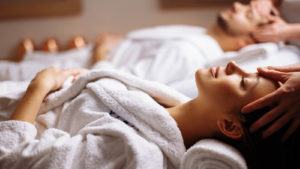Photo of a woman and man in white robes, laying down relaxing at a spa