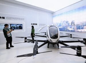 An image of a lifesize white and black pilotable drone display in China with a man taking a picture of a woman in front of it.