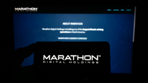 Person holding mobile phone with logo of American company Marathon Digital Holdings Inc. on screen in front of web page. Focus on phone display. Unmodified photo. MARA stock