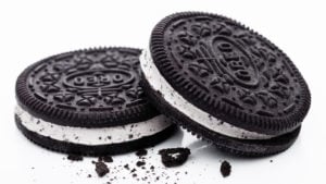 A zoomed in image of one Oreo cookie leaning on another Oreo cookie with cookie crumbles in front and a white background.
