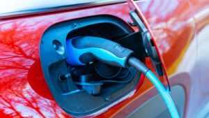 Closeup photo of red electric vehicle being charged with blue and black charger plugged into charging port. undervalued EV stocks. Top-Rated EV Charging stocks