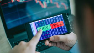 Stocks to buy: smartphone with the words "buy" and "sell" displayed on the screen. The user's finger is about to press buy. Stock charts are in the background of the image. Momentum Stocks. S&P 600 Stocks to Buy. breakthrough stocks. Mario Gabbeli stocks