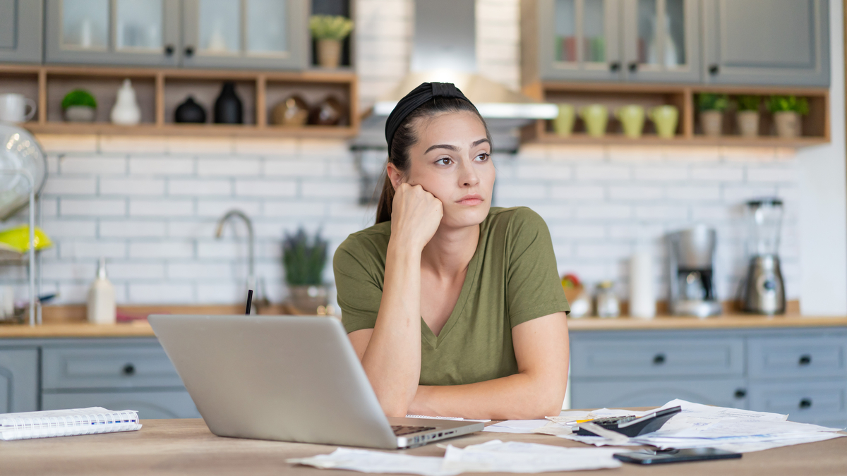 An investor with a worried look leans on a counter with a laptop.