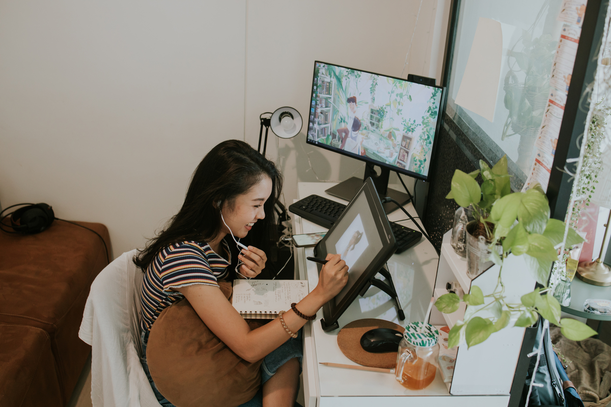 A person seated at a home workspace interacts with multiple computing devices.