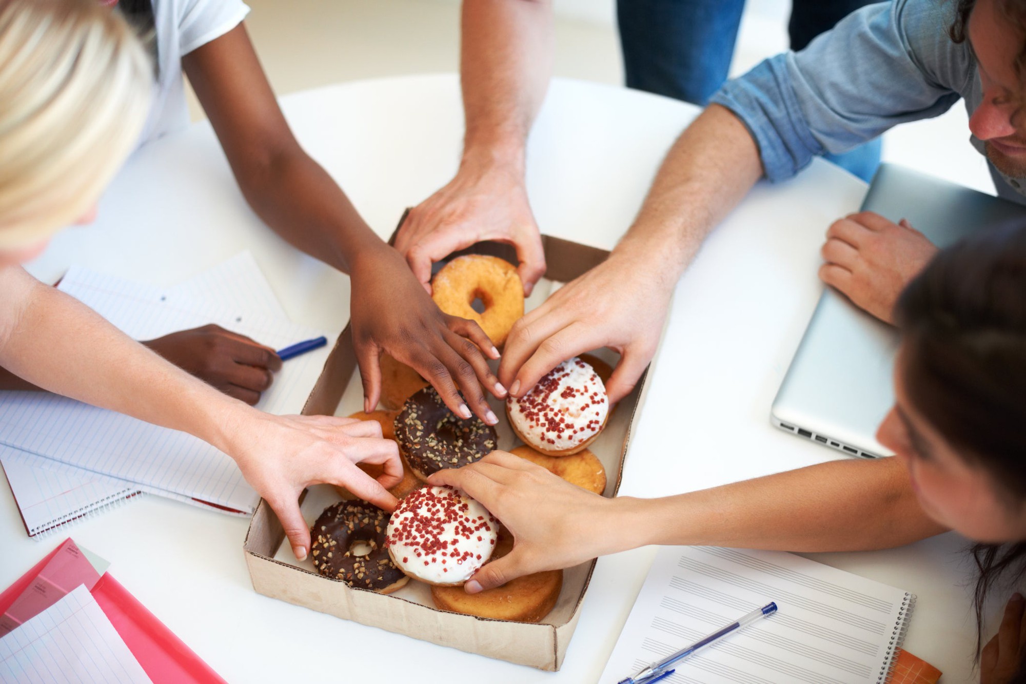 Hands grabbing donuts from a box.
