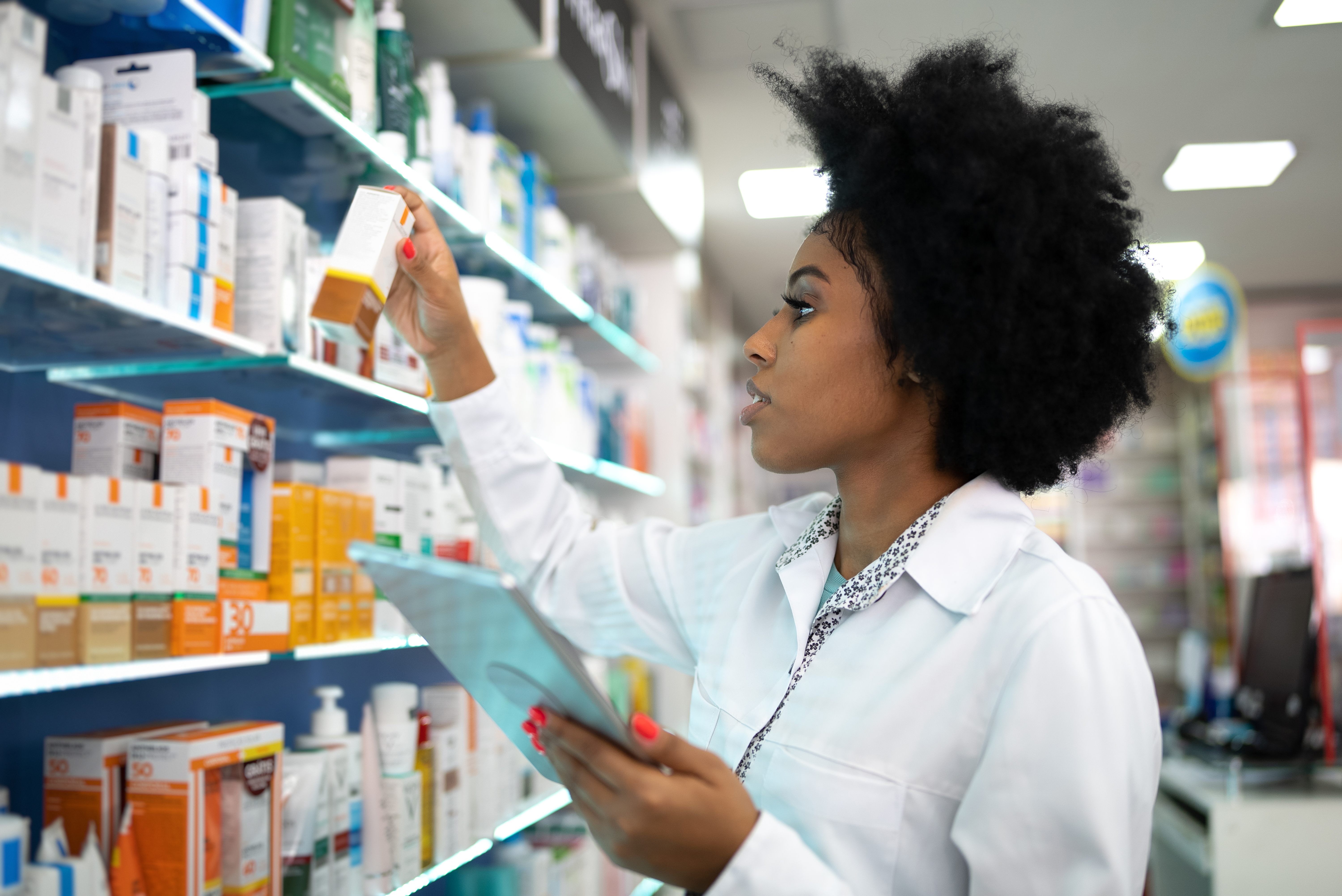 A person checking medicine on a shelf in a pharmacy.