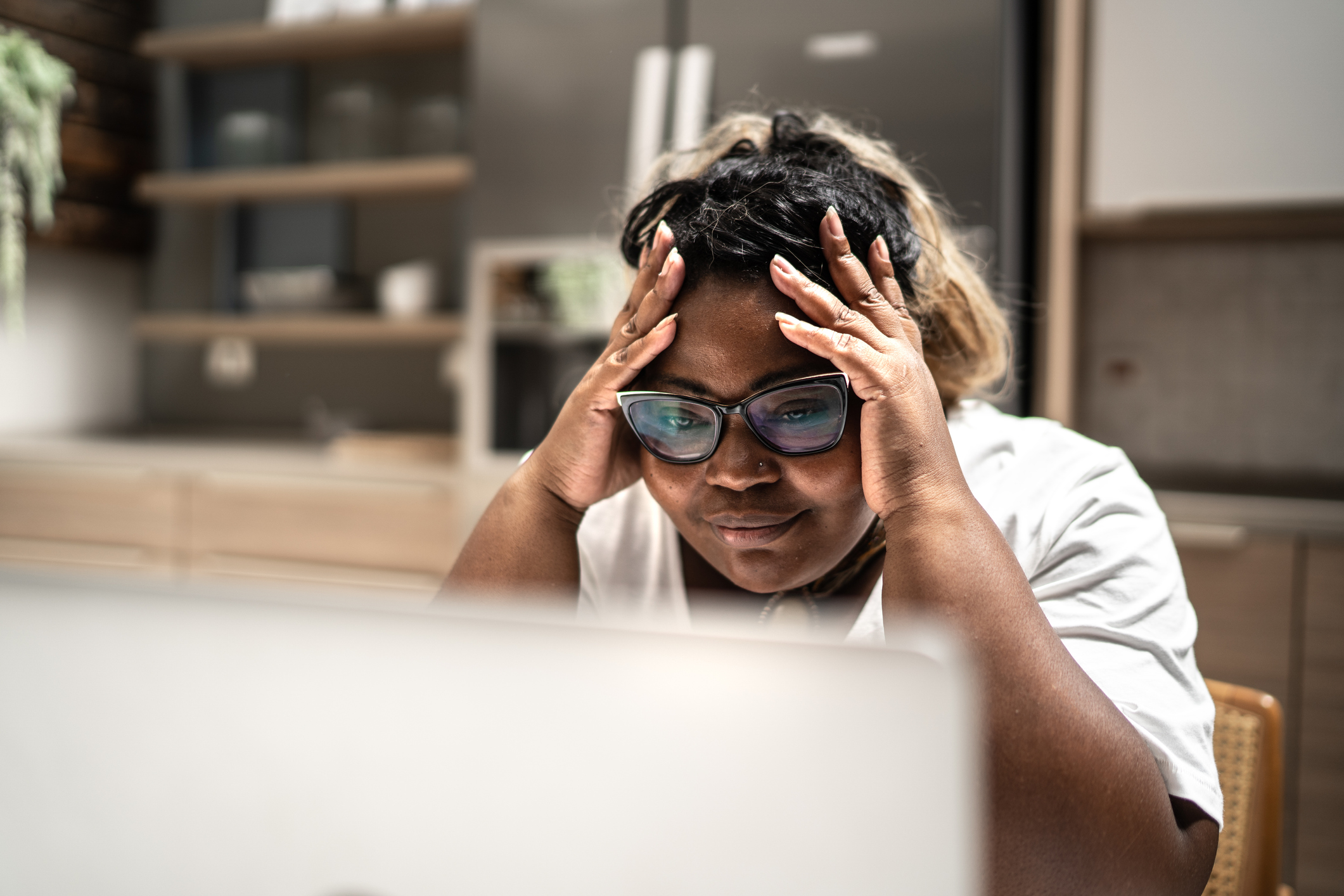 Person looking at laptop screen with head in hands.